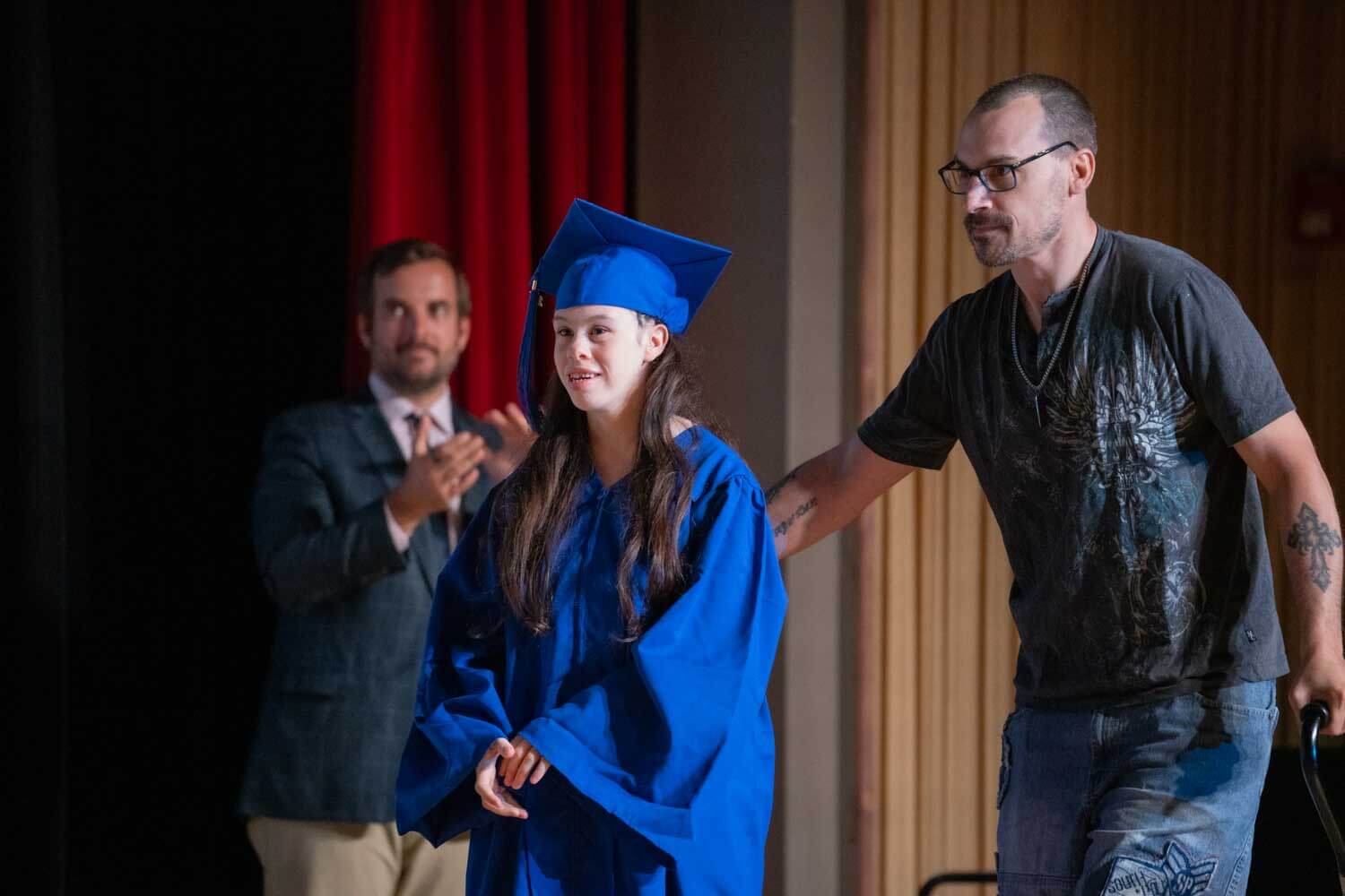 Naag da'yar oo huwan shaadhka qalin-jabinta buluuga ah iyo koofiyadda waxaa hagaya masraxa nin.