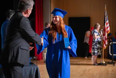 Gabadh yar oo koofiyad buluug ah xidhan iyo goon buluug ah ayaa dhoolla caddaynaysa iyadoo nin ku gacan qaadaysa masraxa xaflad qalin jabin ah.