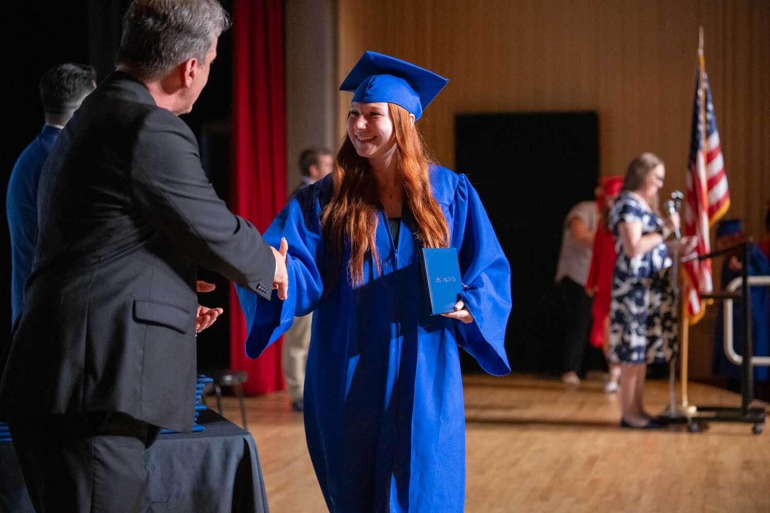 Gabadh yar oo koofiyad buluug ah xidhan iyo goon buluug ah ayaa dhoolla caddaynaysa iyadoo nin ku gacan qaadaysa masraxa xaflad qalin jabin ah.