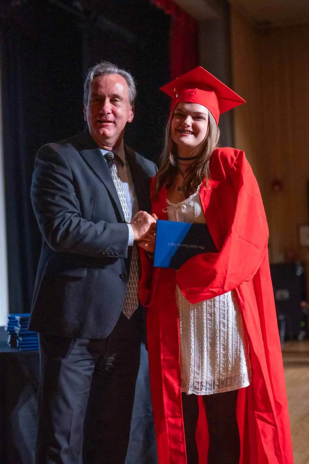 Gabar qalin jabisay oo koofiyad cas iyo gown xidhan ayaa dhoolla caddaynaysa intay salaantay nin suudh xidhan oo masraxa saaran, oo shahaado sita.